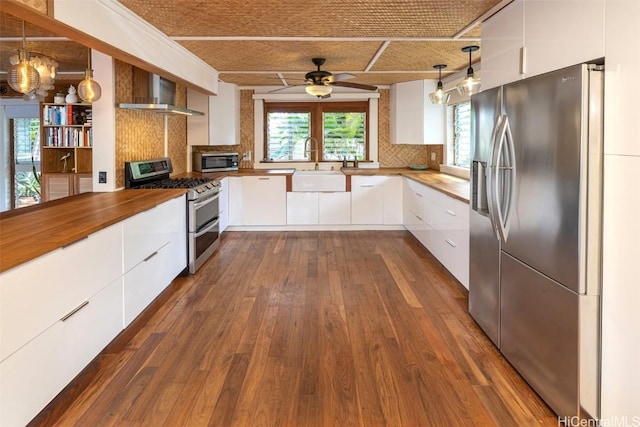 kitchen featuring pendant lighting, appliances with stainless steel finishes, white cabinets, wall chimney range hood, and sink