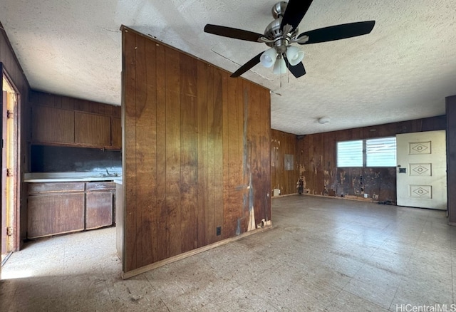 unfurnished living room featuring ceiling fan and wood walls