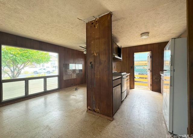 kitchen featuring stainless steel range, white refrigerator, wood walls, ceiling fan, and dark brown cabinets