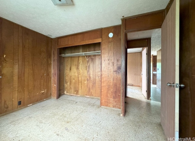 unfurnished bedroom with a closet, wooden walls, and a textured ceiling