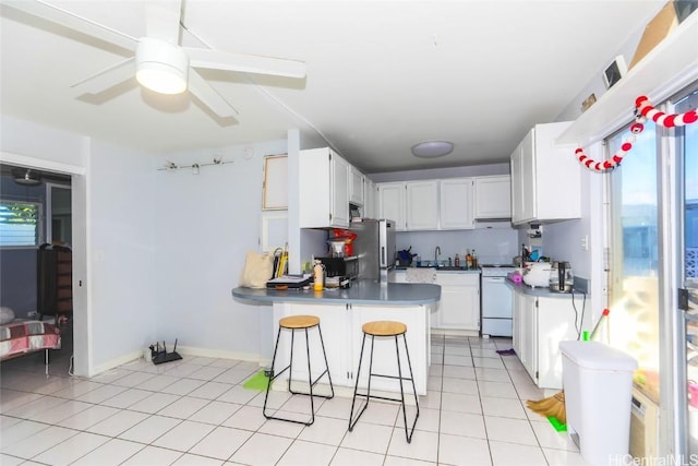 kitchen with ceiling fan, stove, kitchen peninsula, a kitchen bar, and white cabinetry