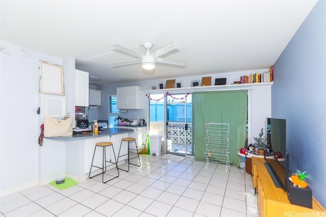 kitchen featuring ceiling fan, a breakfast bar, kitchen peninsula, white cabinetry, and light tile patterned floors