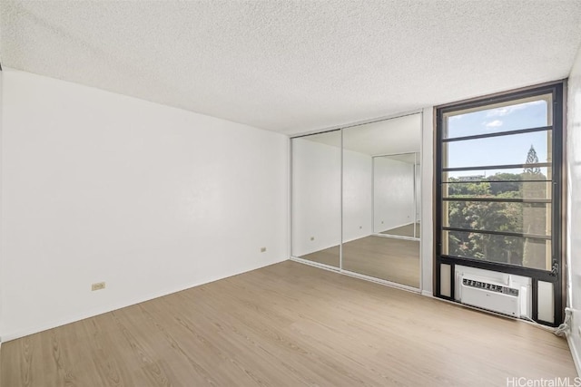 unfurnished bedroom featuring expansive windows, a textured ceiling, a closet, and light hardwood / wood-style flooring