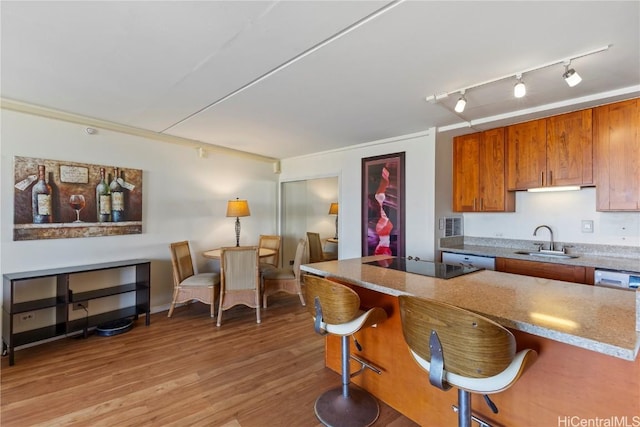 kitchen featuring black electric stovetop, light hardwood / wood-style floors, sink, crown molding, and a breakfast bar area