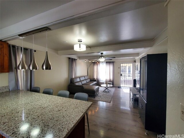 kitchen with ceiling fan, hanging light fixtures, light stone countertops, a kitchen bar, and dark hardwood / wood-style flooring