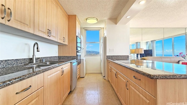 kitchen with stainless steel appliances, sink, a textured ceiling, and dark stone countertops