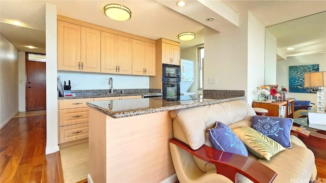 kitchen with kitchen peninsula, sink, black appliances, light brown cabinets, and light hardwood / wood-style flooring