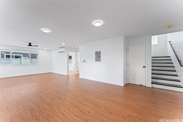 unfurnished living room featuring ceiling fan, electric panel, light hardwood / wood-style flooring, and an AC wall unit