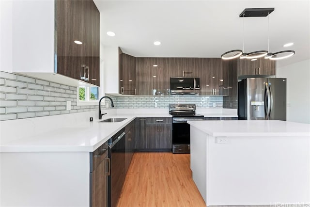 kitchen featuring appliances with stainless steel finishes, decorative light fixtures, tasteful backsplash, sink, and light hardwood / wood-style flooring