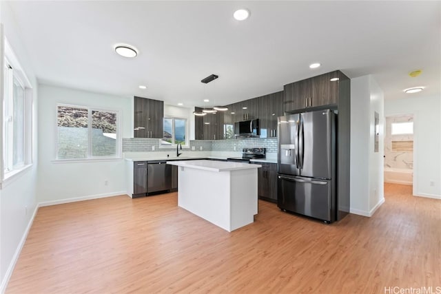 kitchen featuring decorative backsplash, hanging light fixtures, a center island, stainless steel appliances, and light hardwood / wood-style flooring