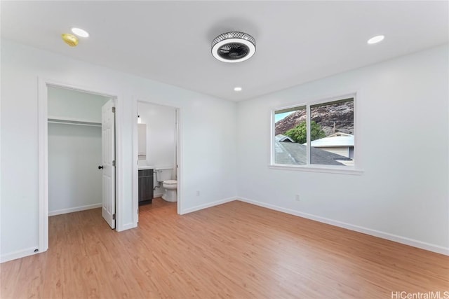 unfurnished bedroom featuring ensuite bathroom, a spacious closet, light wood-type flooring, and a closet