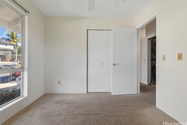 unfurnished bedroom with a closet, stacked washer and dryer, light carpet, and multiple windows