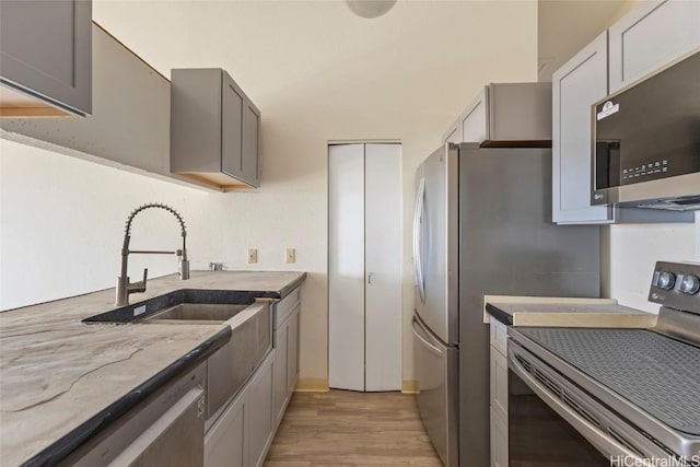 kitchen with stainless steel appliances, gray cabinets, light stone counters, and light hardwood / wood-style floors