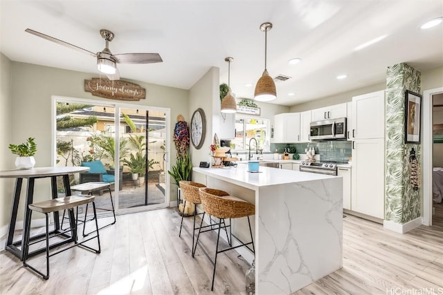 kitchen with stainless steel appliances, pendant lighting, white cabinets, and light hardwood / wood-style floors