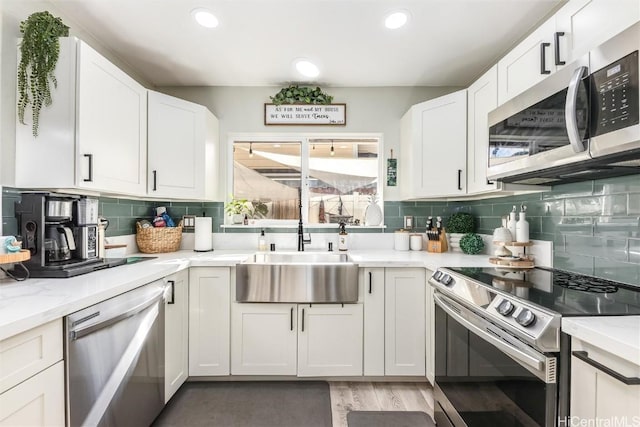 kitchen with stainless steel appliances, white cabinetry, sink, and light stone counters