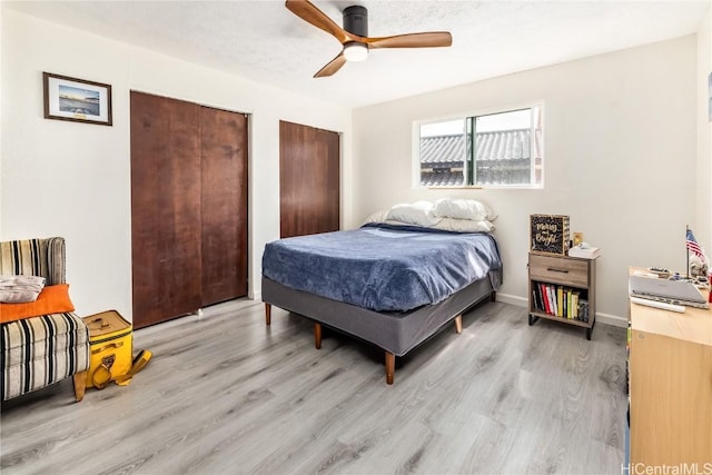 bedroom featuring light wood-type flooring, ceiling fan, multiple closets, and a textured ceiling