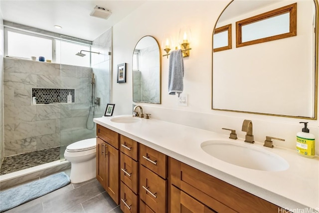 bathroom featuring toilet, vanity, a tile shower, and tile patterned flooring