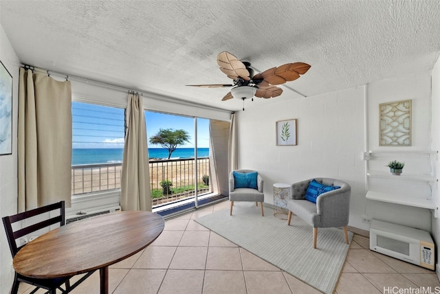 living area featuring light tile patterned flooring, a wealth of natural light, a water view, and a view of the beach