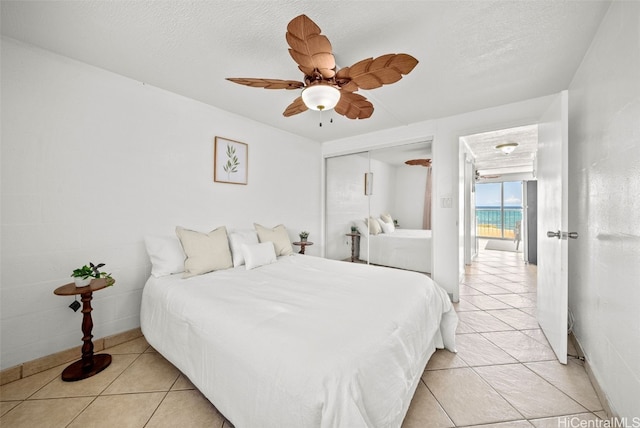 bedroom with ceiling fan, light tile patterned floors, a closet, and a textured ceiling