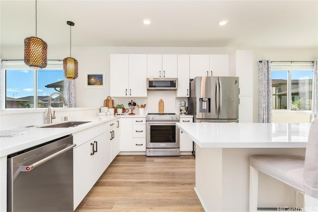 kitchen with appliances with stainless steel finishes, decorative light fixtures, white cabinetry, sink, and light wood-type flooring