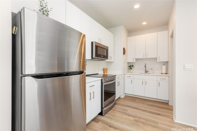 kitchen with appliances with stainless steel finishes, light hardwood / wood-style flooring, white cabinets, and sink