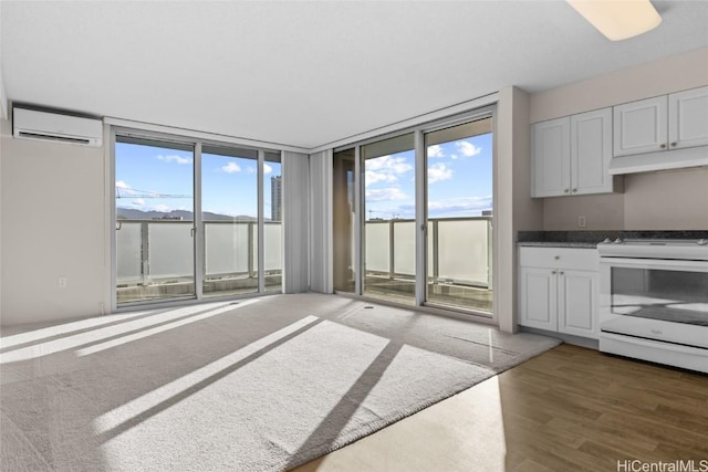 kitchen with an AC wall unit, white electric range, expansive windows, dark wood-type flooring, and white cabinets