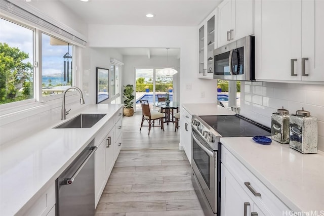 kitchen featuring sink, appliances with stainless steel finishes, white cabinetry, backsplash, and light hardwood / wood-style floors