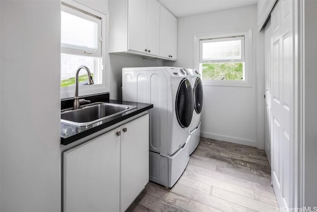 clothes washing area featuring sink, light hardwood / wood-style flooring, cabinets, and washing machine and clothes dryer