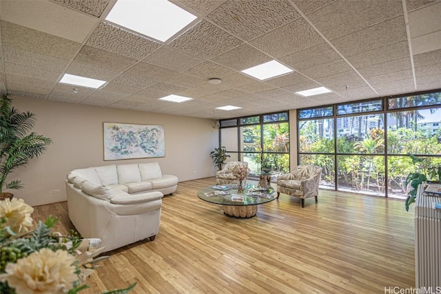 living room featuring wood-type flooring, a drop ceiling, and a wall of windows