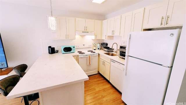 kitchen featuring white appliances, a peninsula, light countertops, under cabinet range hood, and a sink