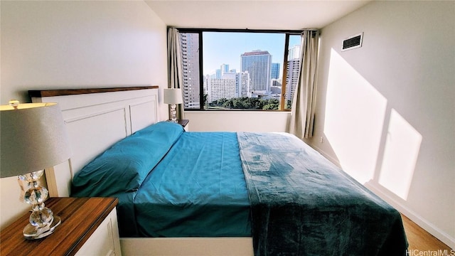 bedroom with wood finished floors, visible vents, and a city view