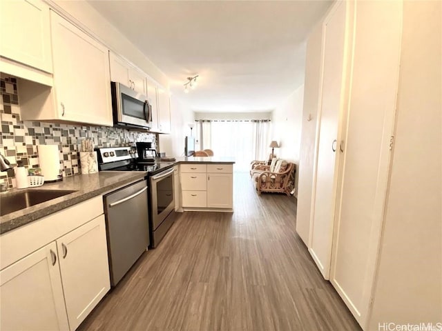 kitchen with tasteful backsplash, kitchen peninsula, sink, white cabinetry, and stainless steel appliances