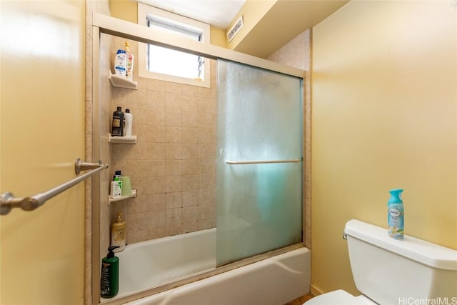 bathroom featuring toilet and shower / bath combination with glass door