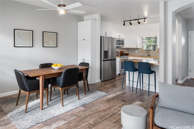 dining space with dark wood-style floors, arched walkways, ceiling fan, and baseboards