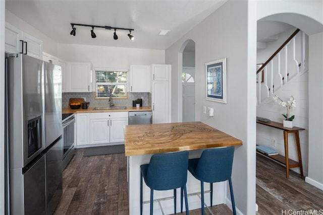 kitchen featuring tasteful backsplash, a kitchen breakfast bar, white cabinets, stainless steel appliances, and wood counters