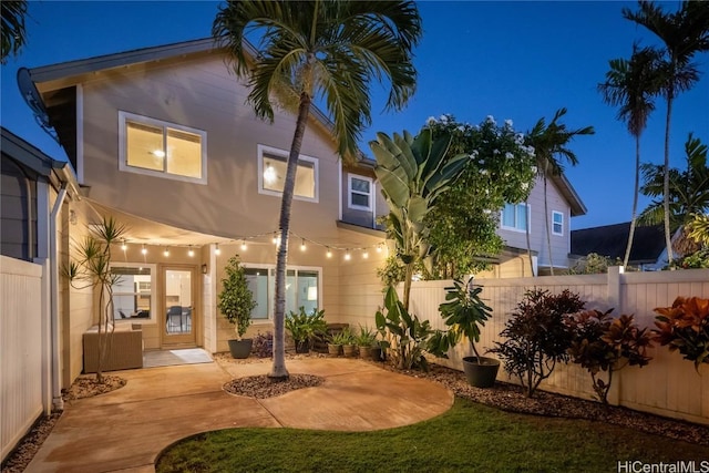 back of house at night featuring a patio area, fence, and stucco siding