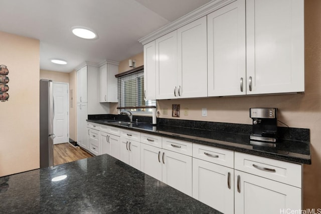 kitchen featuring dark stone countertops, light hardwood / wood-style floors, sink, stainless steel refrigerator, and white cabinets