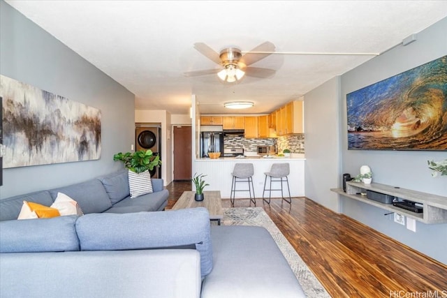 living room with stacked washer / dryer, ceiling fan, and dark hardwood / wood-style flooring