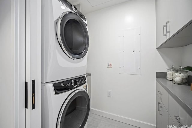 laundry room featuring stacked washing maching and dryer, cabinets, and electric panel