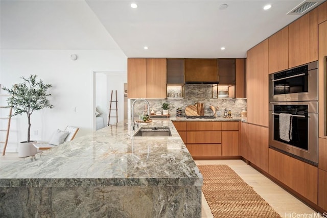 kitchen featuring appliances with stainless steel finishes, decorative backsplash, light hardwood / wood-style flooring, light stone counters, and sink