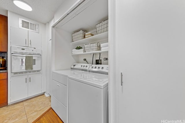 clothes washing area featuring light tile patterned floors, a textured ceiling, and washer and clothes dryer