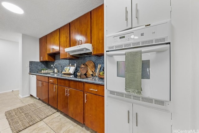 kitchen featuring white appliances, a textured ceiling, sink, backsplash, and light tile patterned floors