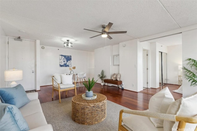 living room with a textured ceiling, dark wood-type flooring, and ceiling fan