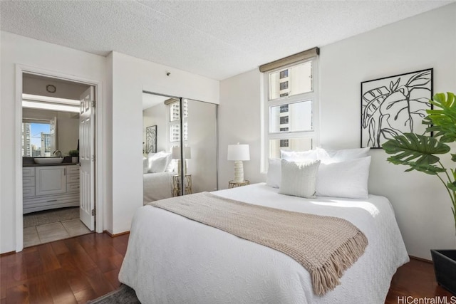 bedroom featuring a textured ceiling, ensuite bath, dark hardwood / wood-style flooring, sink, and a closet