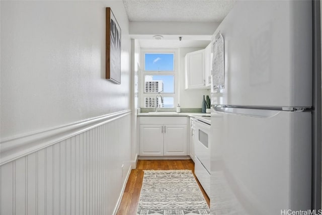 kitchen with white fridge, light hardwood / wood-style floors, a textured ceiling, white cabinets, and sink