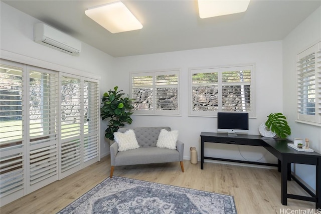 sitting room with a wall mounted air conditioner, plenty of natural light, and light wood-type flooring