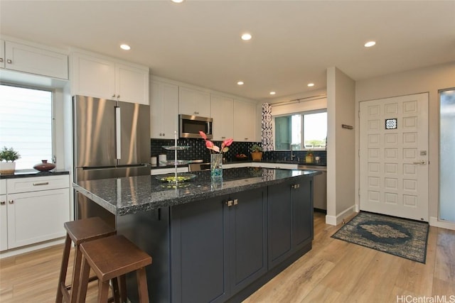 kitchen with appliances with stainless steel finishes, white cabinetry, backsplash, light hardwood / wood-style floors, and dark stone counters