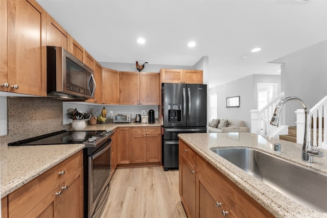 kitchen featuring tasteful backsplash, sink, light wood-type flooring, light stone countertops, and stainless steel appliances