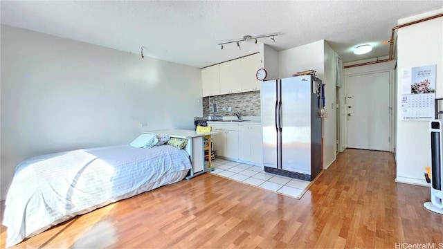 bedroom featuring sink, track lighting, a textured ceiling, light hardwood / wood-style floors, and stainless steel refrigerator