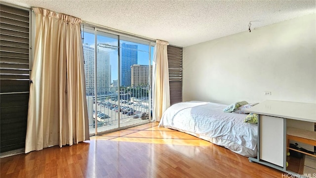 bedroom featuring a textured ceiling, hardwood / wood-style flooring, floor to ceiling windows, access to exterior, and multiple windows